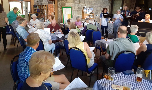 Adults gathered in the Tower Room for a beer and hymns and pimms musical social event.